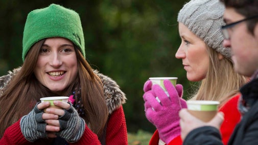 Visitors in hats and gloves with hot drinks outside at Upton House and Gardens, Warwickshire